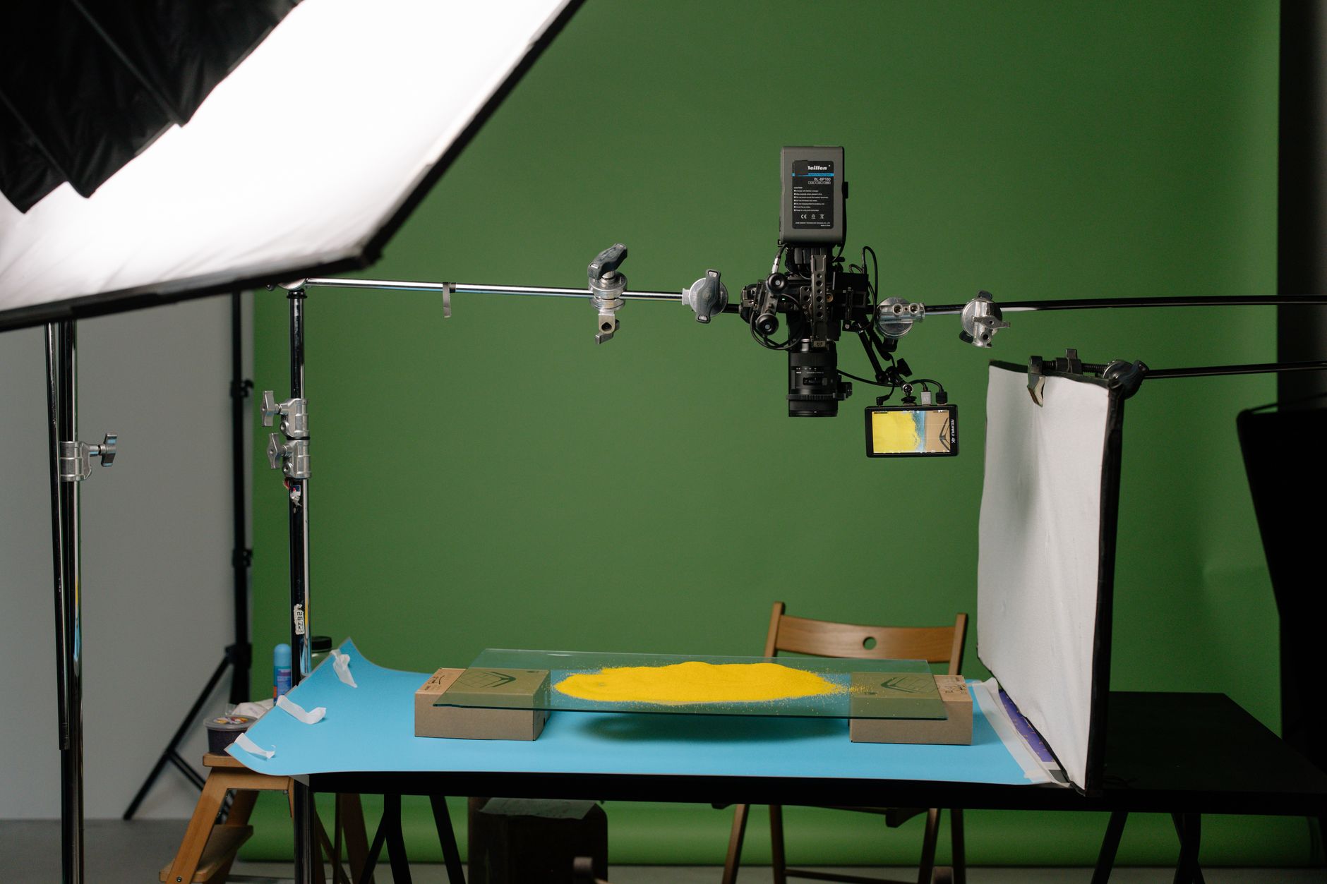 Een opnamestudio met een grote softbox, een camera aan een giek boven een tafel en een groene achtergrond.